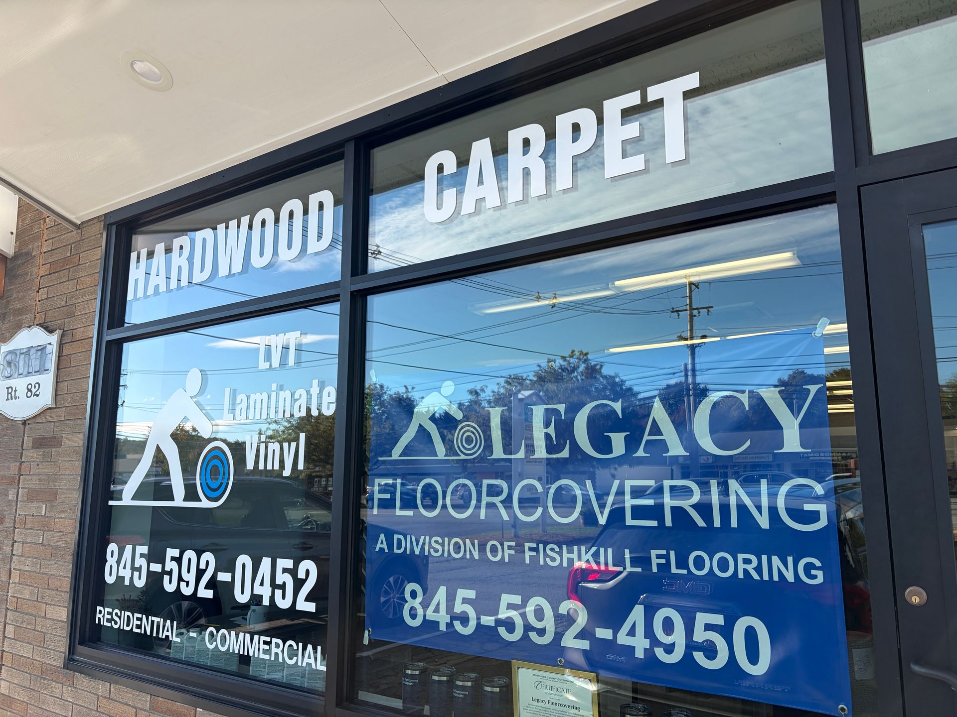 Window signage for Legacy Floorcovering, advertising hardwood, carpet, and contact info, storefront exterior.