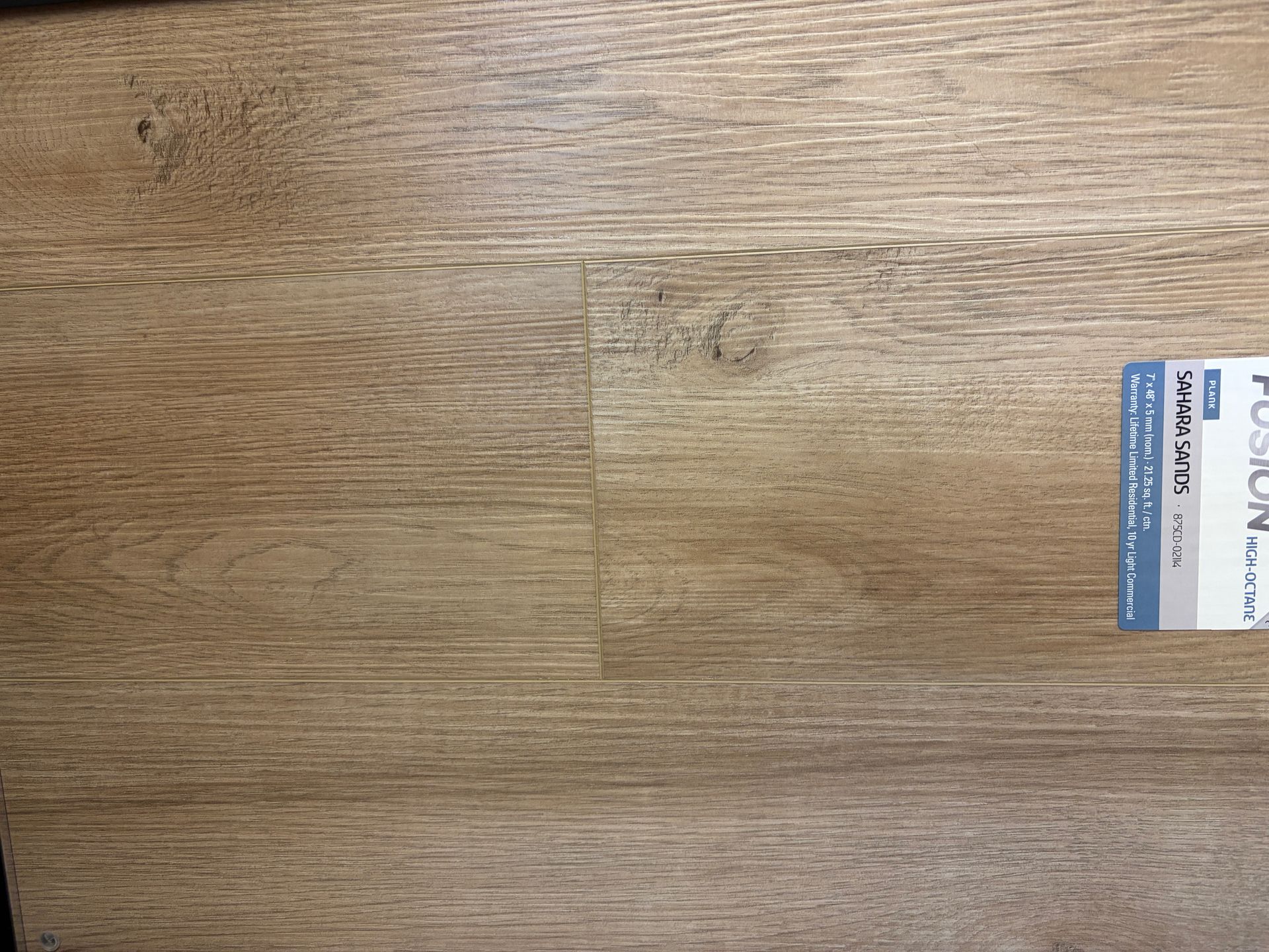 Close-up of light brown wood flooring with a small product label in the corner.