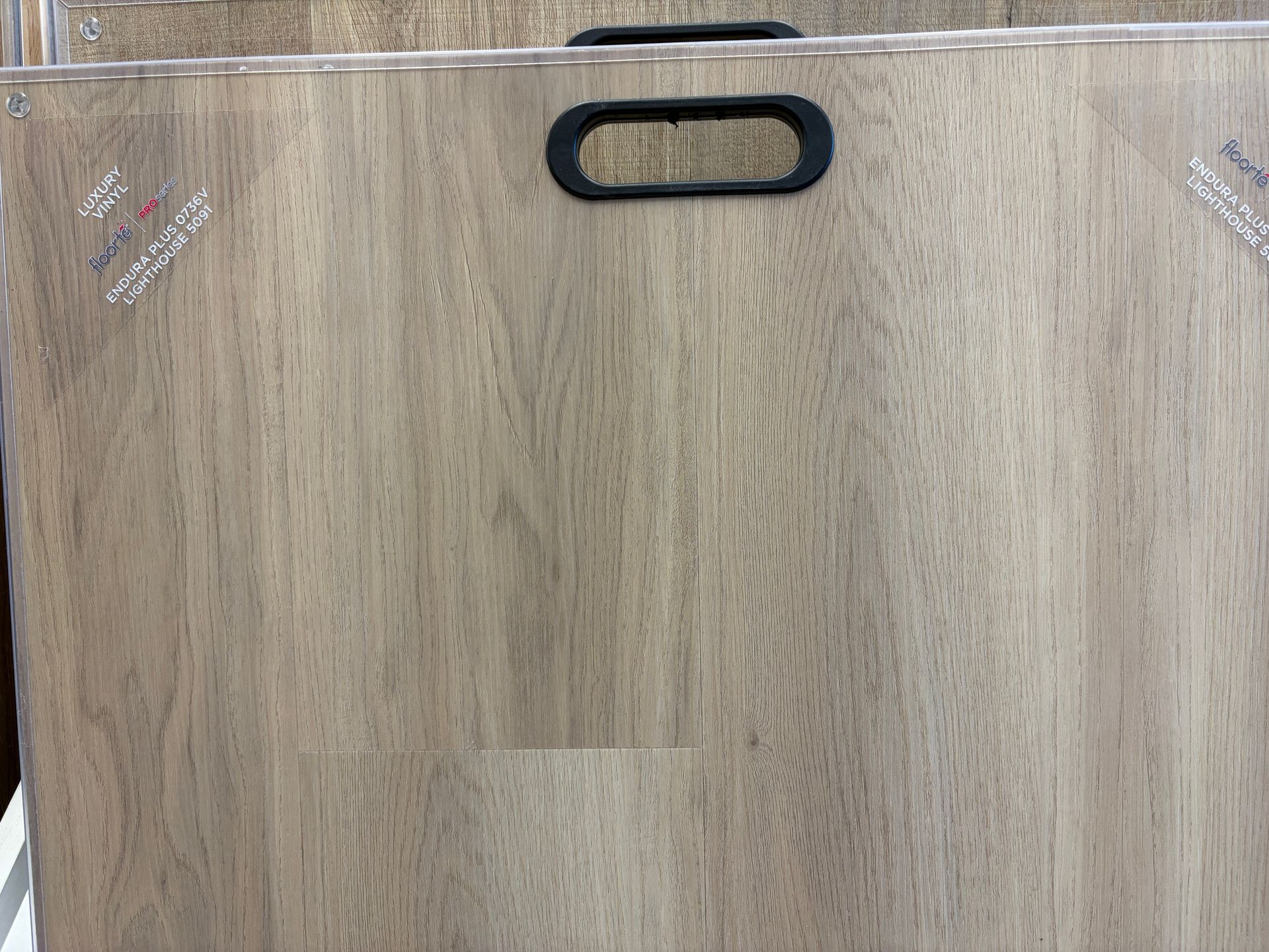 Light brown wood-look flooring sample with black handle and protective wrap.