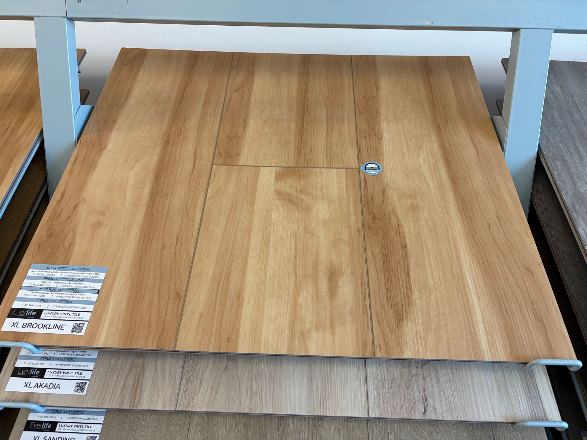 Wooden flooring sample on a display rack. Light brown planks with a small inset and a metal fastener.