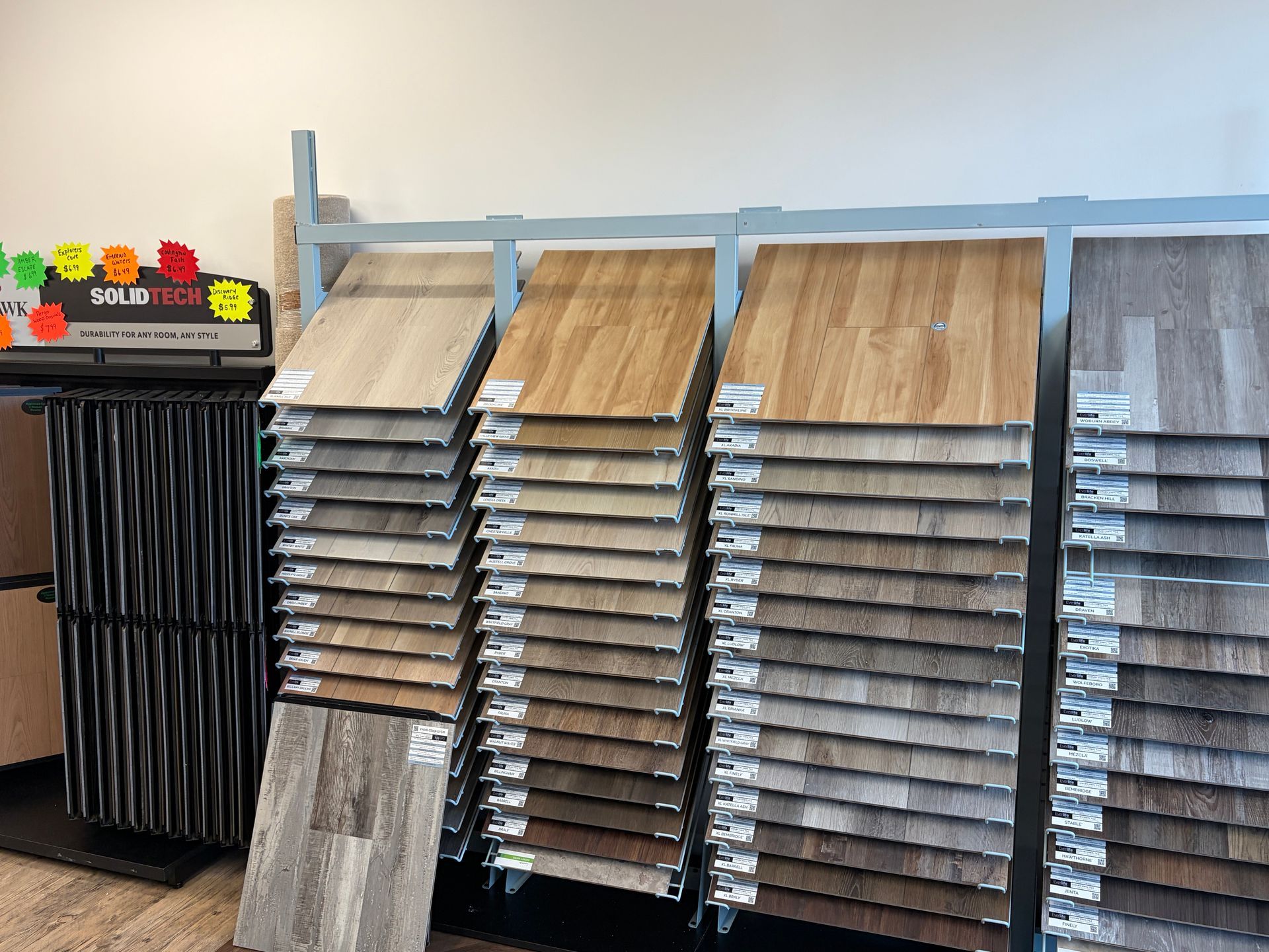 Display of various flooring samples in a showroom, arranged on metal racks, showcasing different wood-look textures and colors.