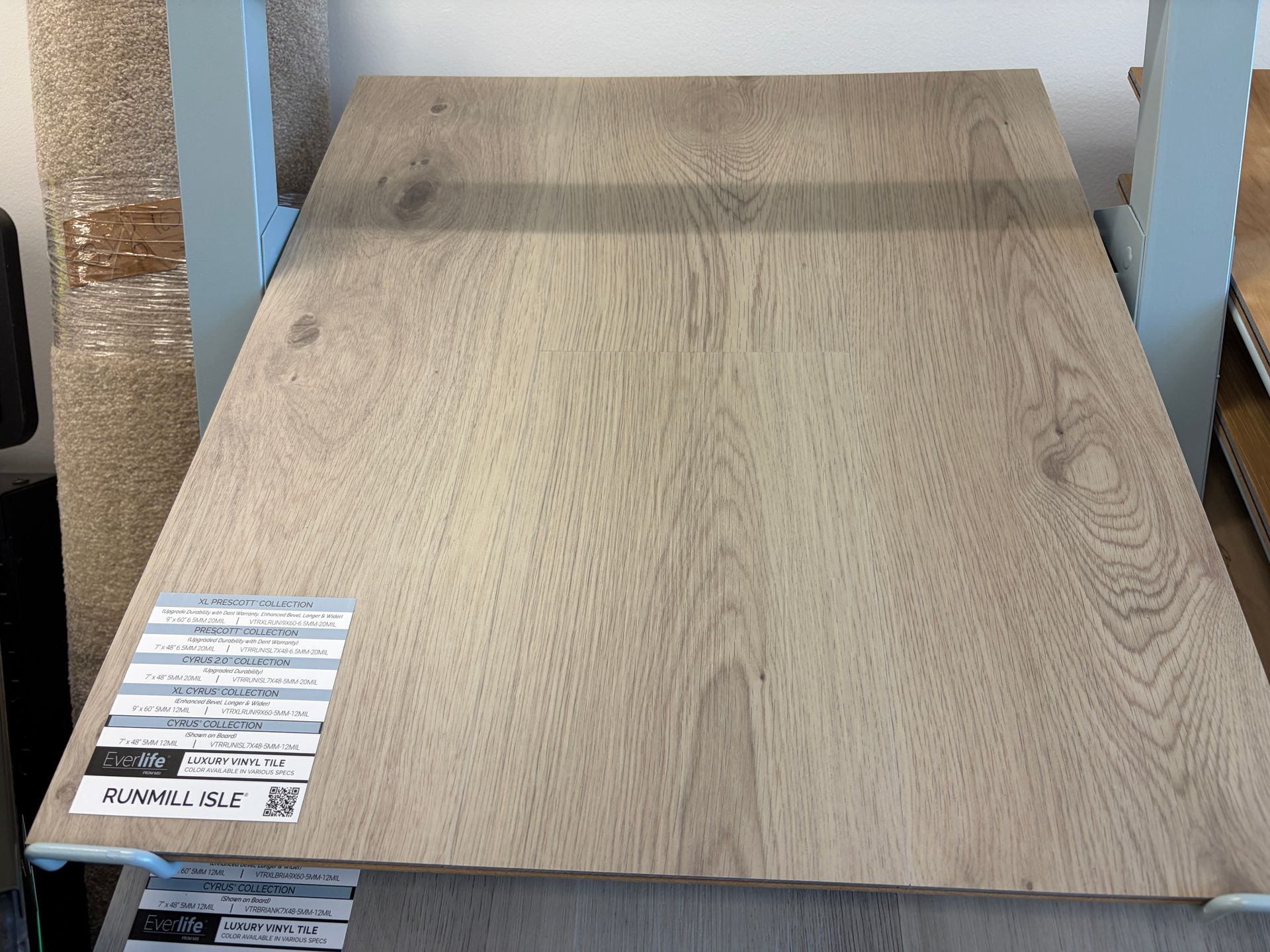 Wooden flooring sample on a display rack, light brown with wood grain pattern.