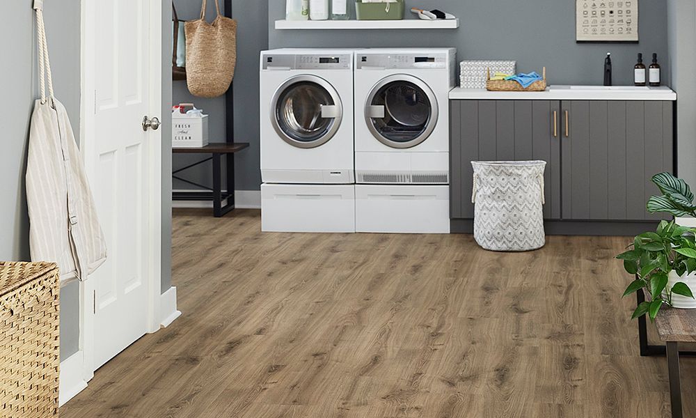 Laundry room with washer, dryer, cabinets, and wood-look flooring. A laundry basket sits on the floor.