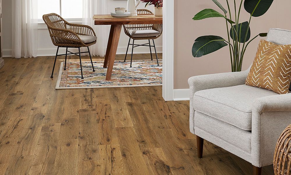 Hardwood flooring in a dining area with a table, chairs, rug, and armchair with pillow.