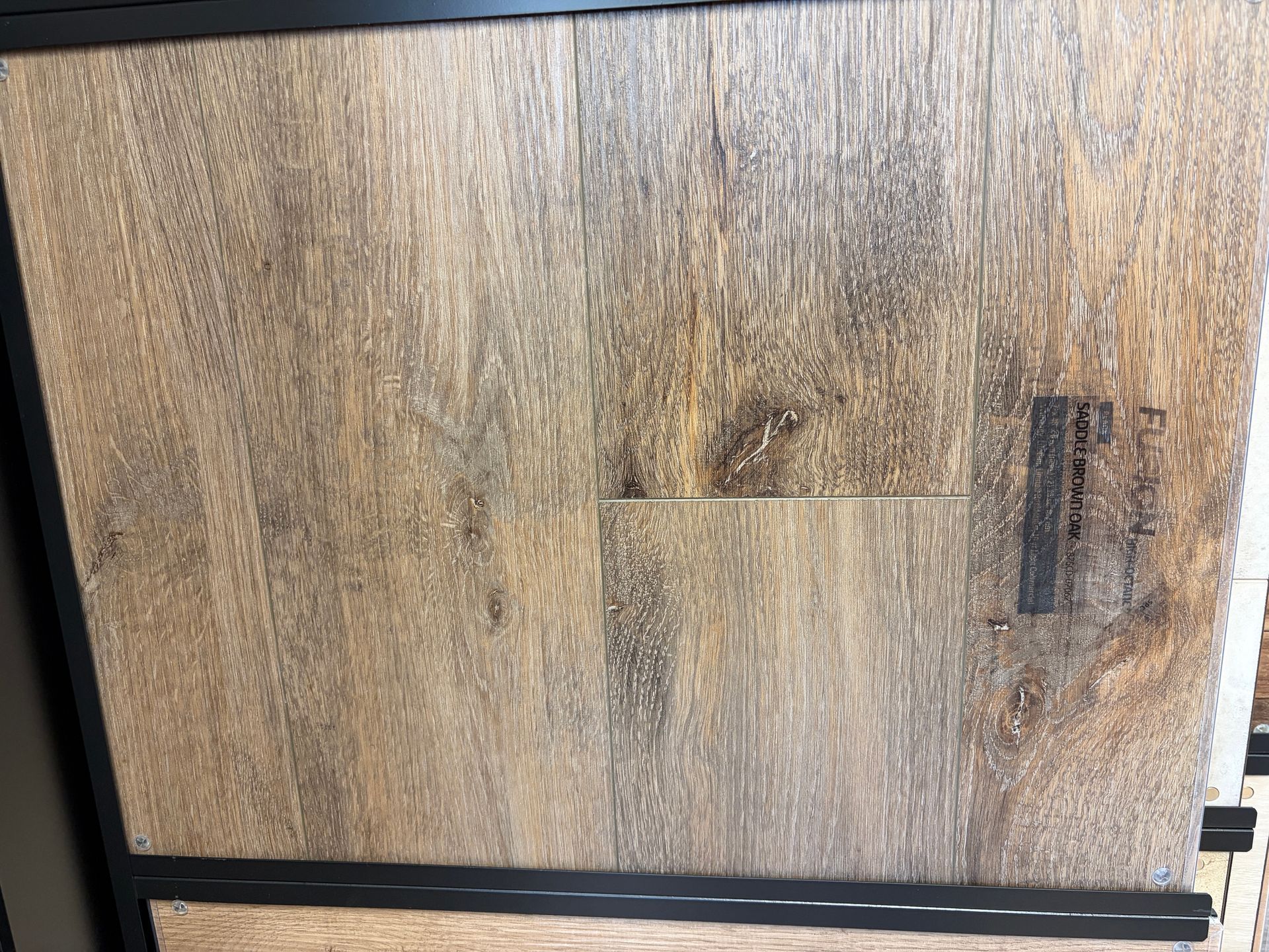 Wooden flooring sample, light brown with dark graining, framed in black.