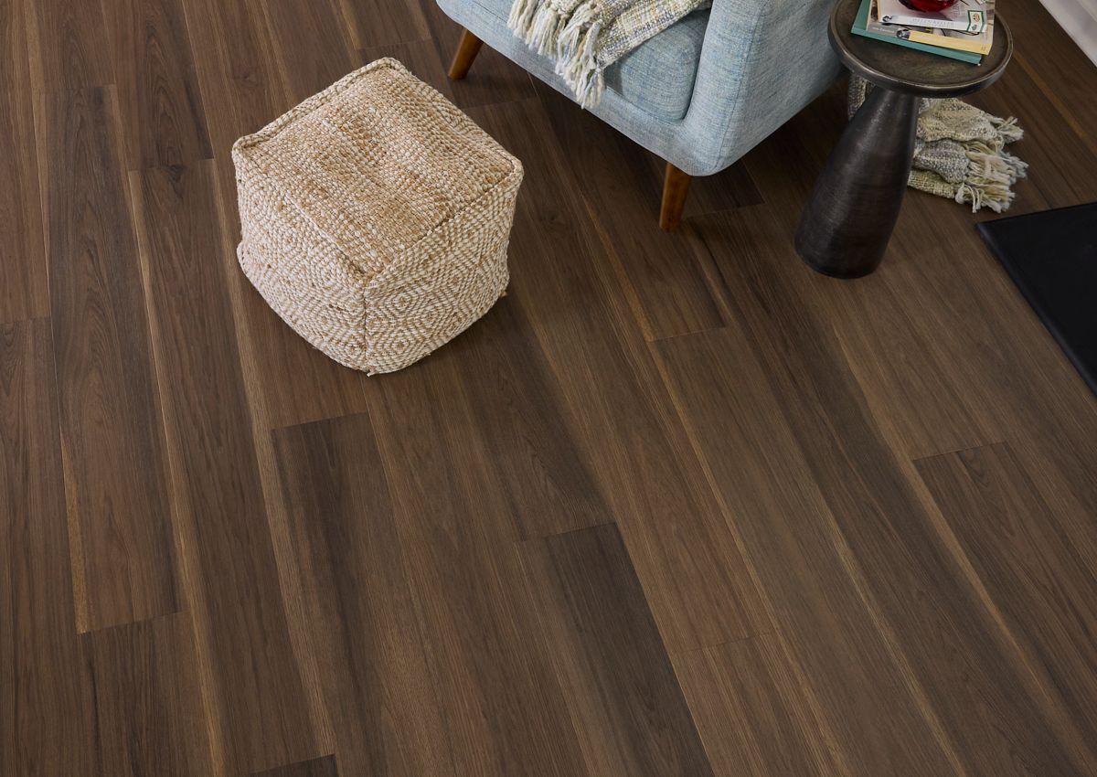 Dark hardwood floor, cozy living space. Tan ottoman, blue armchair, side table with books.