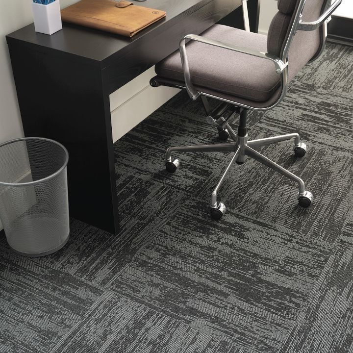 Desk with a black surface, grey office chair, trash can, and patterned carpet.