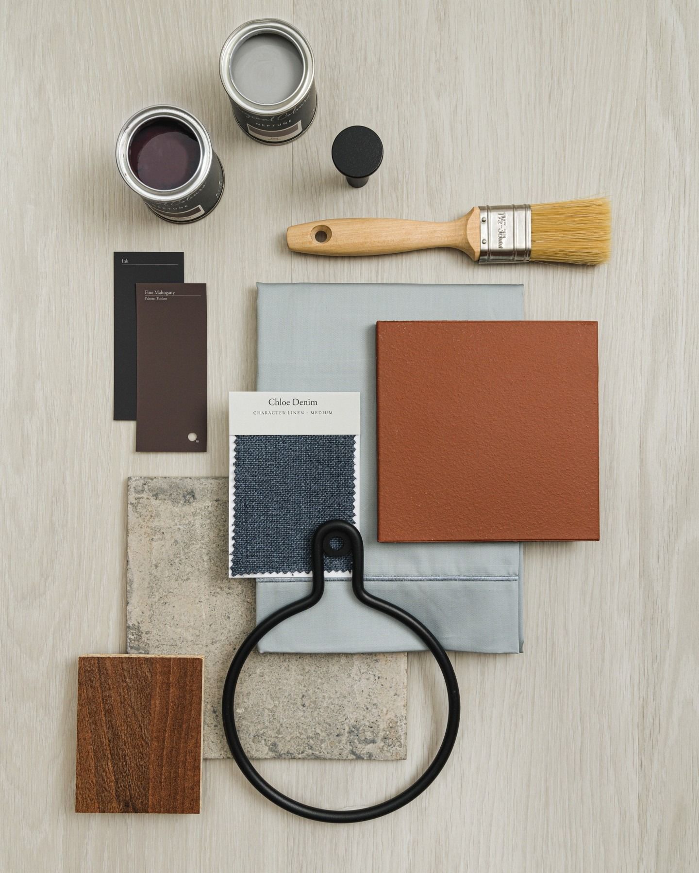 A design mood board with paint cans, swatches of fabric, leather, wood, a brush, and a black handle.