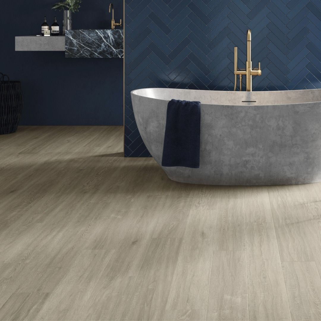 Bathroom with wooden floor, grey bathtub, blue herringbone tile, and gold faucet.