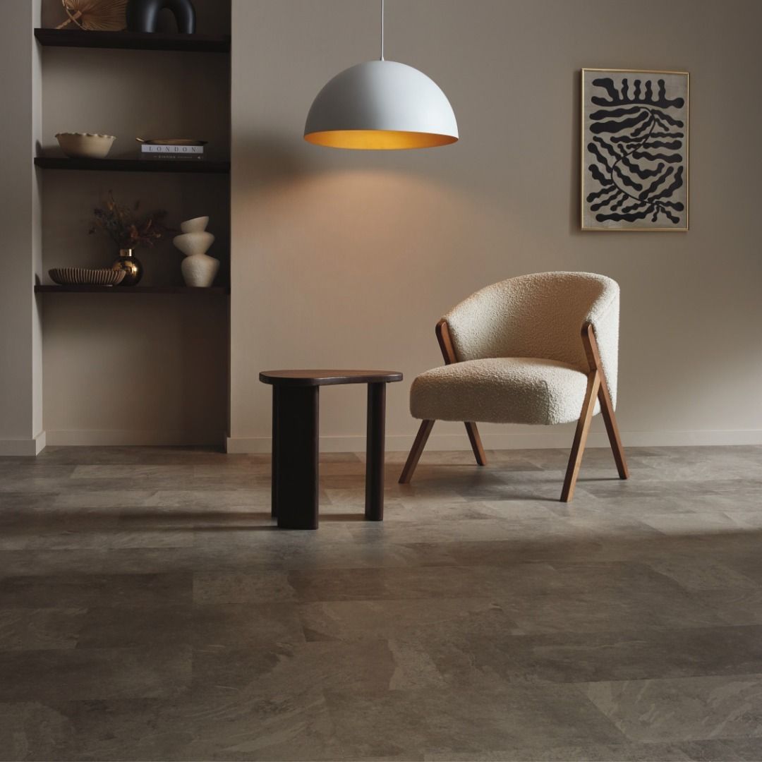 Cozy living room with cream armchair, dark side table, shelves, and abstract art under a pendant light.