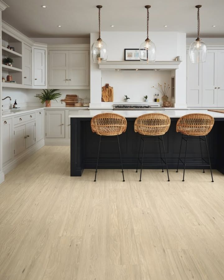Light wood-floored kitchen with white cabinets, dark island, wicker stools, and pendant lights.