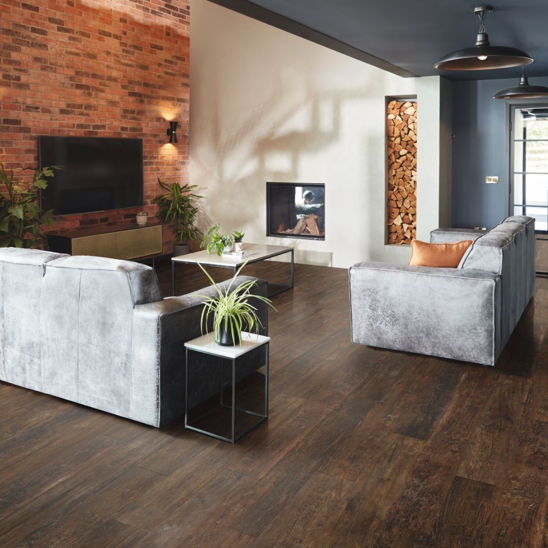 Living room with brick wall, fireplace, two gray sofas, dark wood floor, and overhead lighting.