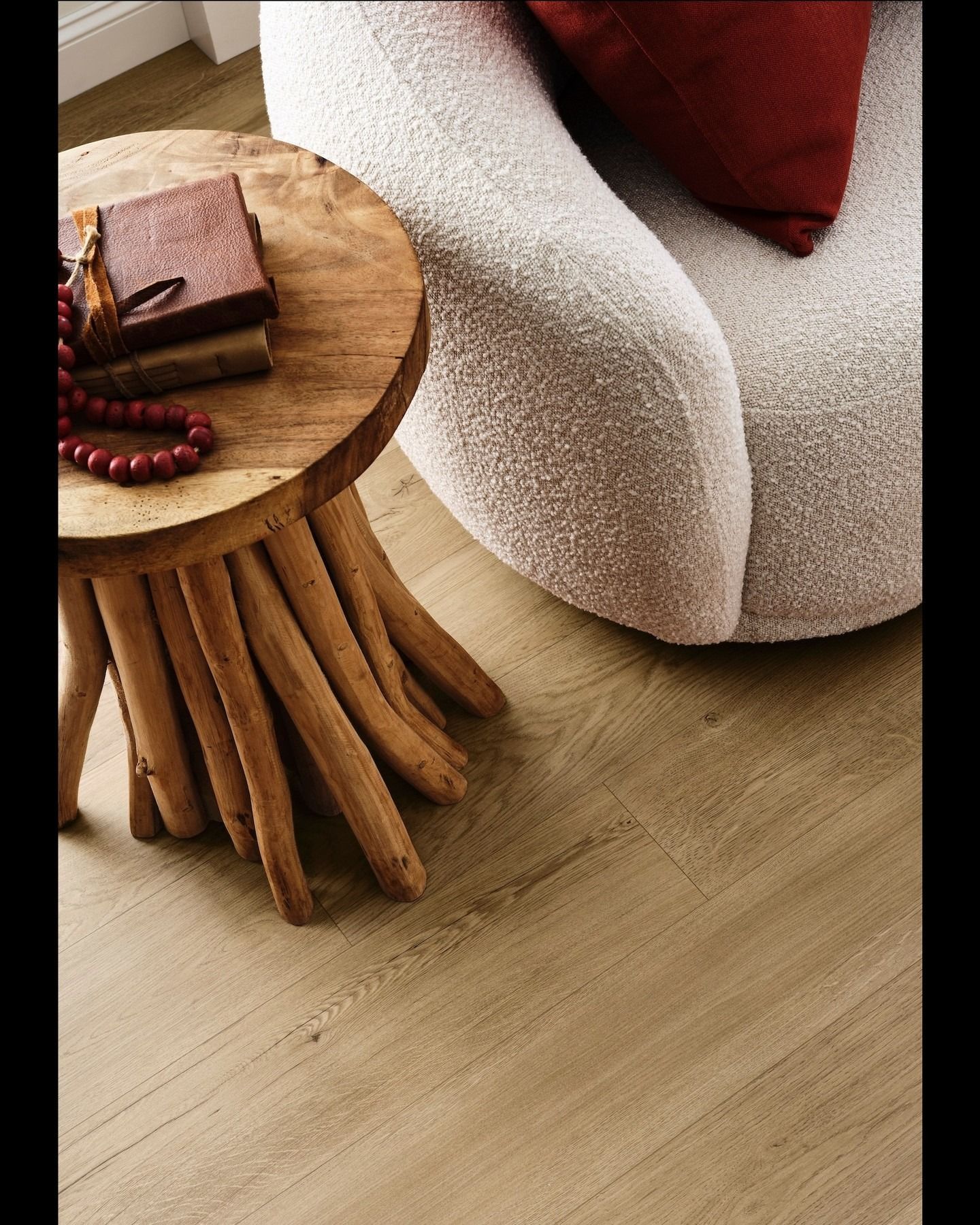 Wooden side table with books and beads, next to a textured white armchair and light wood floor.