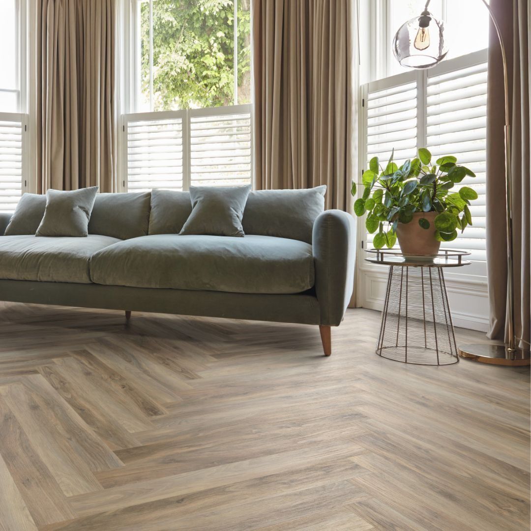 Living room with beige herringbone floor, blue sofa, window with shutters, and a potted plant.