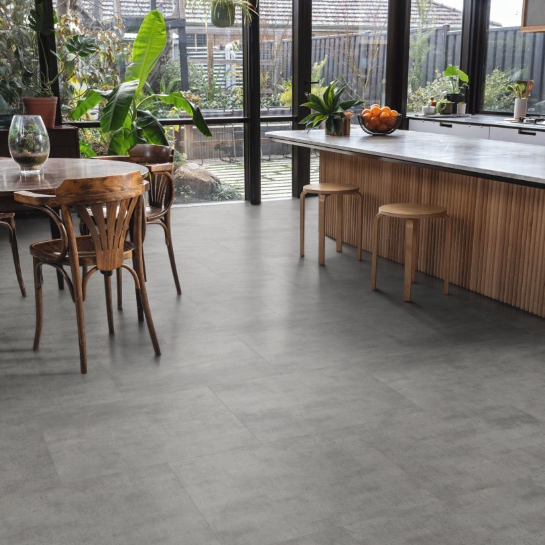 A modern kitchen with a dining table and chairs, and a kitchen island. The floor is gray. Large windows look out to a garden.