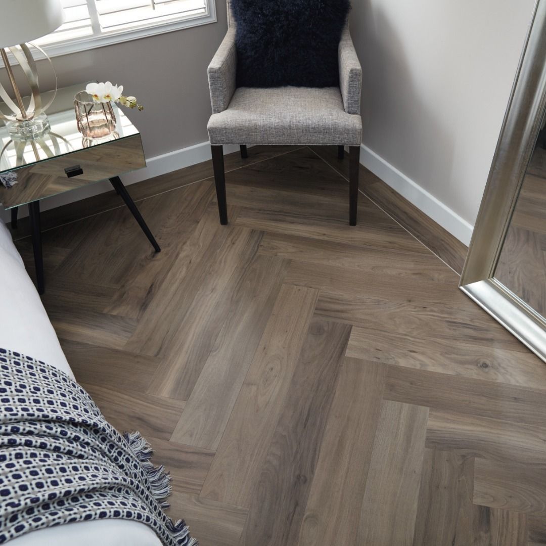 Herringbone wood floor in a corner of a room with a chair, side table, and mirror.