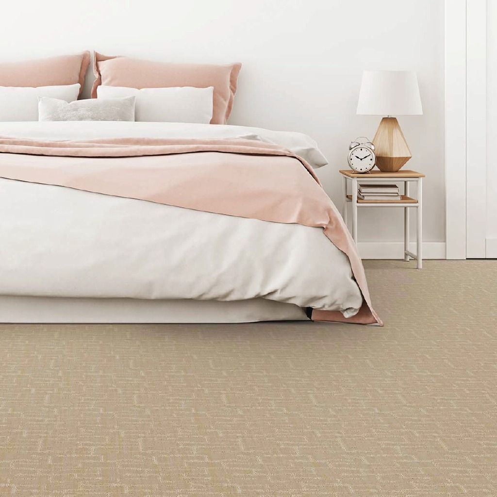 Bedroom with a bed, bedding, a bedside table, lamp, and neutral patterned carpet.