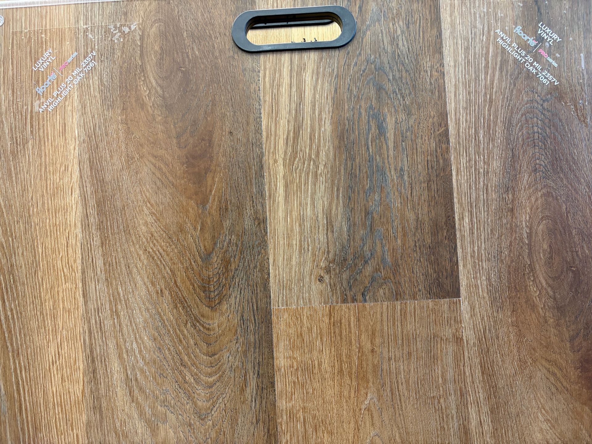 Brown wooden flooring sample with a black handle at the top.