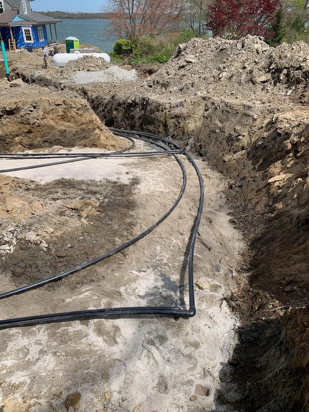 Trenches at a construction site with black cables laid across concrete and dirt mounds.