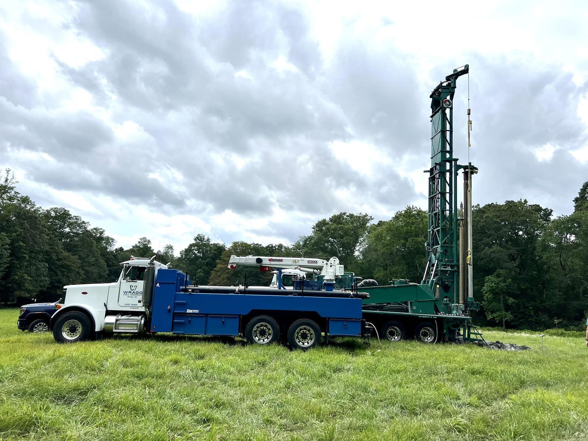 White and blue drilling truck parked in a grassy field under cloudy skies