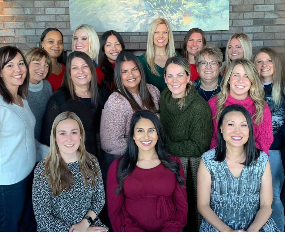 Group of smiling women posing for a photo in front of a brick wall.