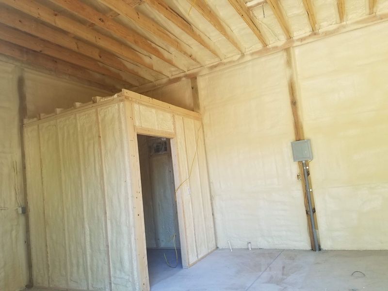 Interior of a building with spray foam insulation on the walls and ceiling; a small room with a doorway is present.