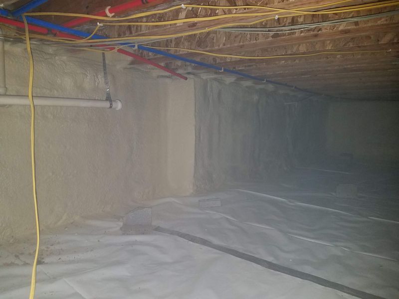 Crawl space with spray foam insulation on walls and a plastic vapor barrier on the ground.