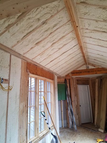 Interior view of a room under construction, walls and ceiling insulated with spray foam, wooden frames, window and door frames.