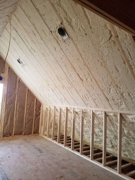 Interior view of an attic with wooden framing and spray foam insulation covering the walls and ceiling.