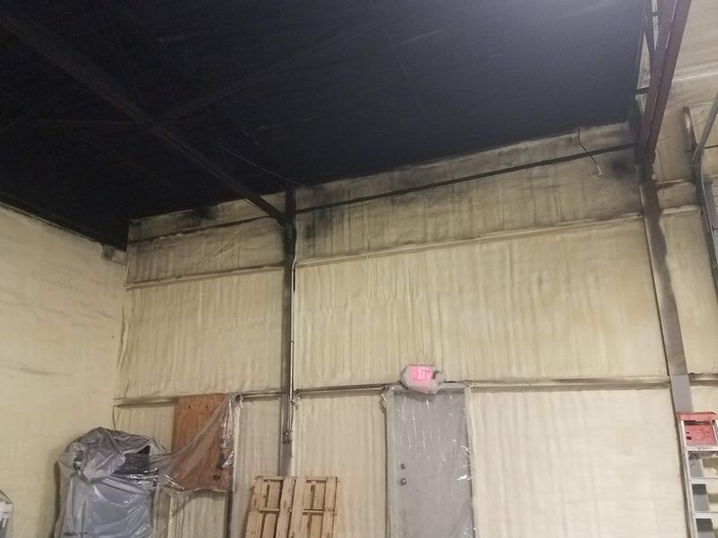 Interior view of a building with beige insulated walls, a black ceiling, and wooden supports.