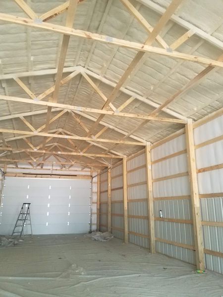 Interior of a large, new building with exposed wooden beams and spray foam insulation. A garage door is visible.