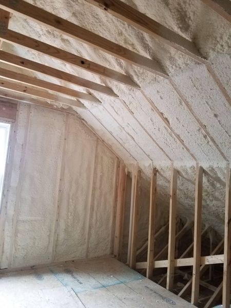 Interior view of attic with spray foam insulation between wooden beams.