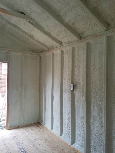 Interior of a room insulated with light green spray foam; wood floors and a light switch visible.