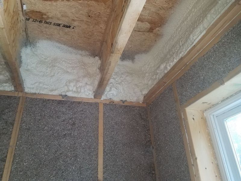 Interior view of a room with spray foam insulation on the ceiling and dark textured insulation on the walls.