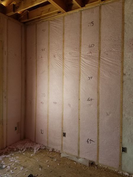 Pink insulation installed between wooden studs in a room under construction.