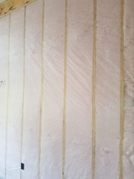 Wall with insulation between wooden studs, covered in plastic sheeting.