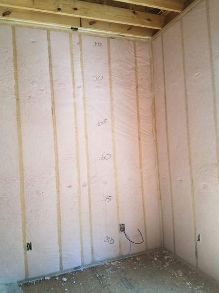 Interior wall under construction with insulation between wooden studs, marked with numbers.