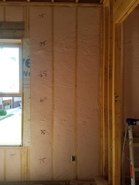 Interior wall under construction; pink insulation between wooden studs; window on the left; room framing on the right.