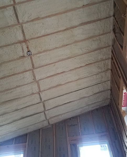 Spray foam insulation on an angled ceiling with wooden beams and framing.