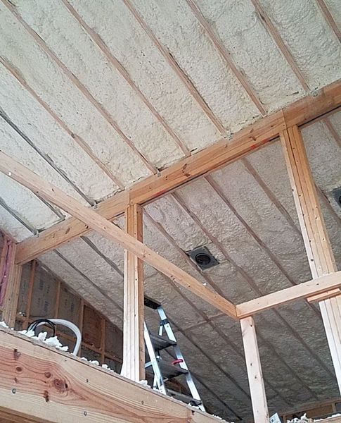 Spray foam insulation fills a wooden attic frame, covering beams and rafters.