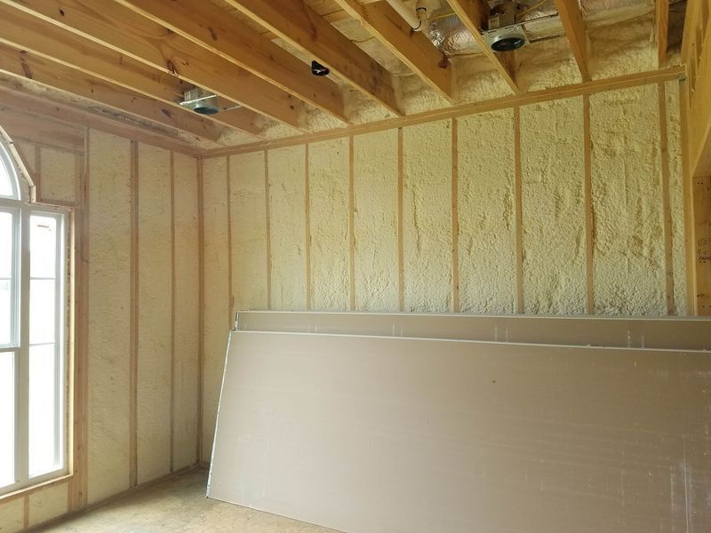 Interior of a room under construction with spray foam insulation in the walls. Drywall sheets lean against an insulated wall.