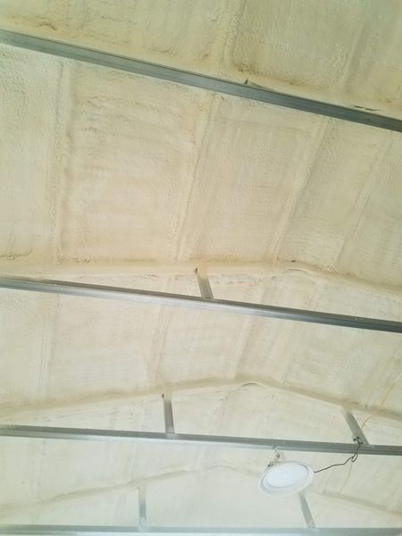 Tan spray foam insulation on a metal-framed ceiling, with a light fixture.