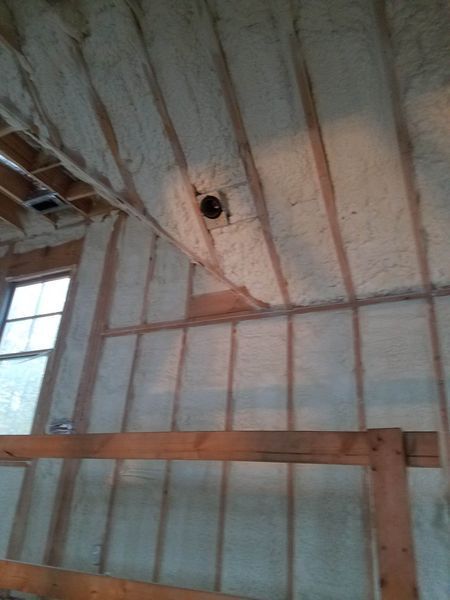 Interior view of a room with exposed wooden beams and walls covered in light-colored spray foam insulation.