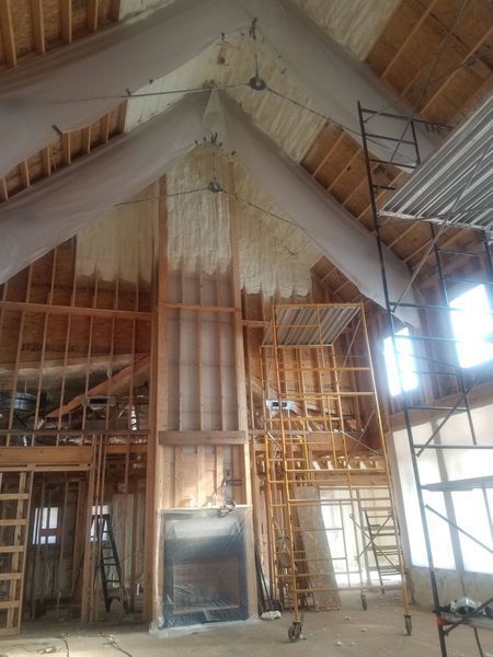 Interior view of a wood-framed building under construction with spray foam insulation on the walls and ceiling.