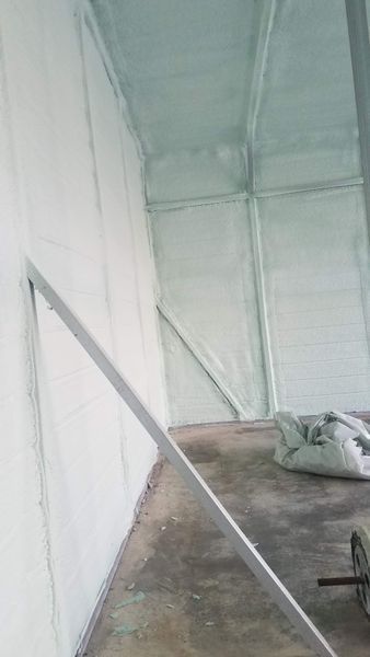 Interior of a structure with white walls and ceiling, covered in insulation. A metal frame leans against the wall.