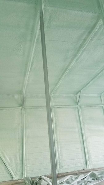 Green spray foam insulation applied to the interior walls and ceiling of a building, covering the framework.