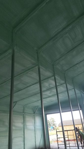 Green spray foam insulation covering the interior walls and ceiling of a building, with metal supports.