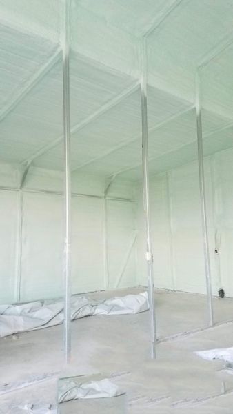 Interior view of a room insulated with green foam. Vertical metal supports extend from floor to ceiling.