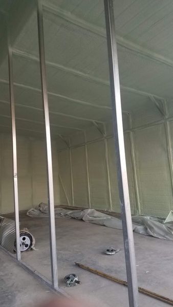 Interior of a building under construction, metal framing, spray foam insulation on walls and ceiling, concrete floor.