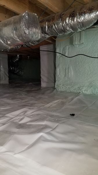 Crawlspace with white vapor barrier, spray foam insulation on foundation walls, and ductwork.